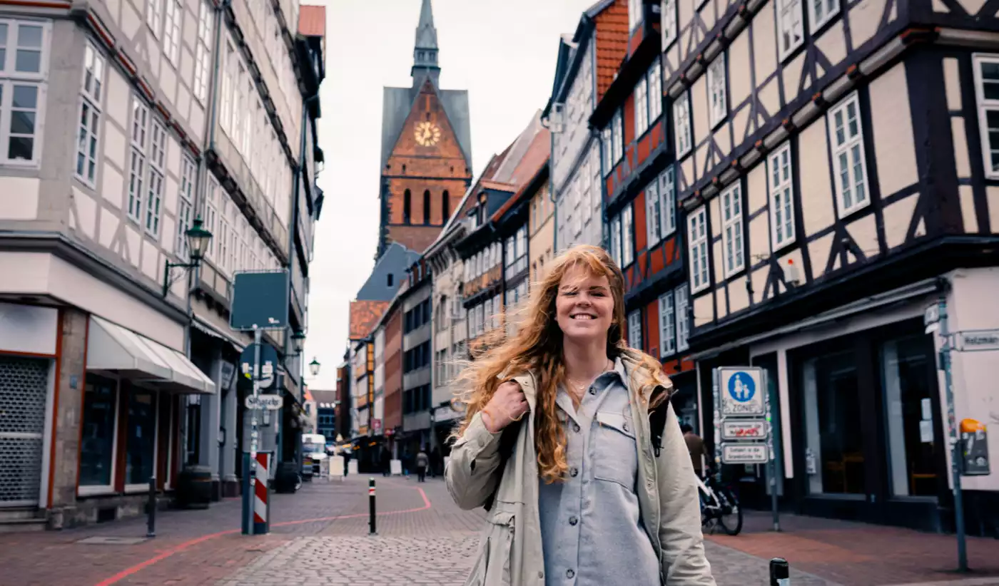 Eine Frau lächelt in die Kamera, im Hintergrund ist die Altstatdt der Stadt Hannover zu erkennen.