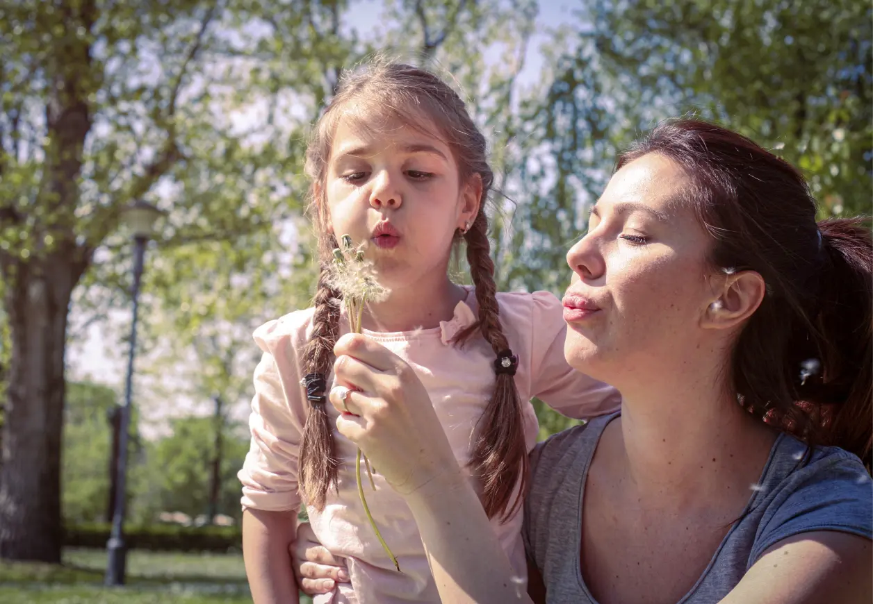 Eine Mutter und ihre Tochter pusten gegen eine Pusteblume.