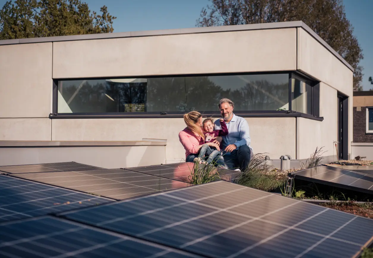 Im Vordergrund sind PV-Module zu sehen. Im Hintergrund eine Familie aus Mann, Frau und Kind, die gemeinsam in die Sonne schauen.