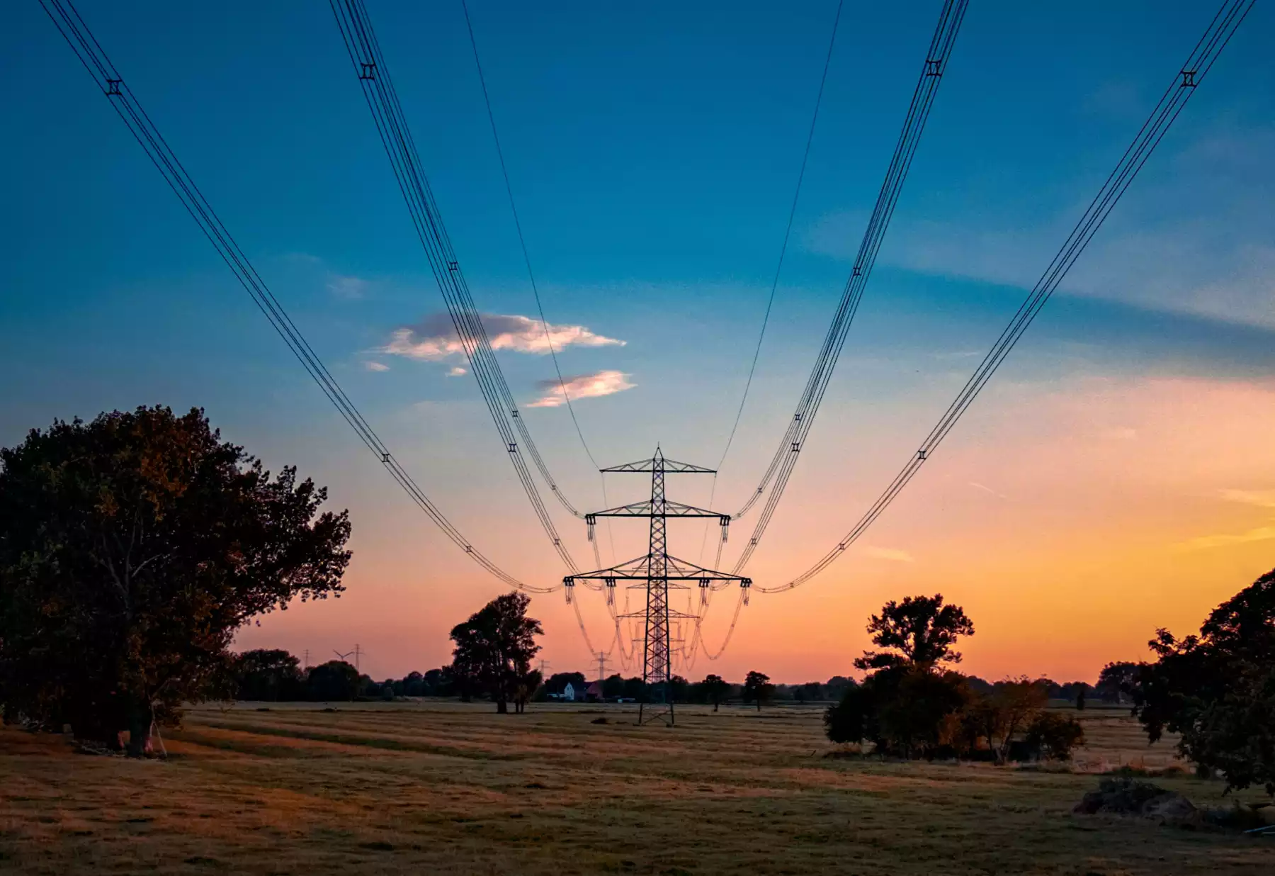 Foto bei Sonnenuntergang unterhalb einer Stromtrasse, die durch eine grüne Landschaft führt.