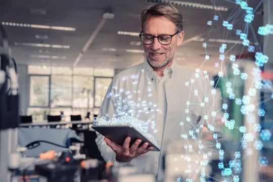 Ein Mann steht im Büro und schaut auf sein Tablet in der Hand.