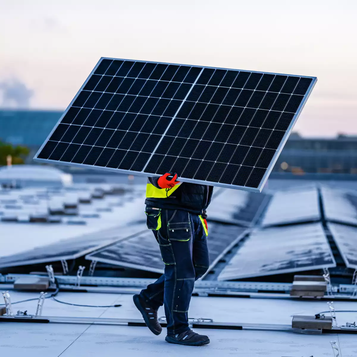 Ein Man trägt ein PV-Modul über ein großes Dach.