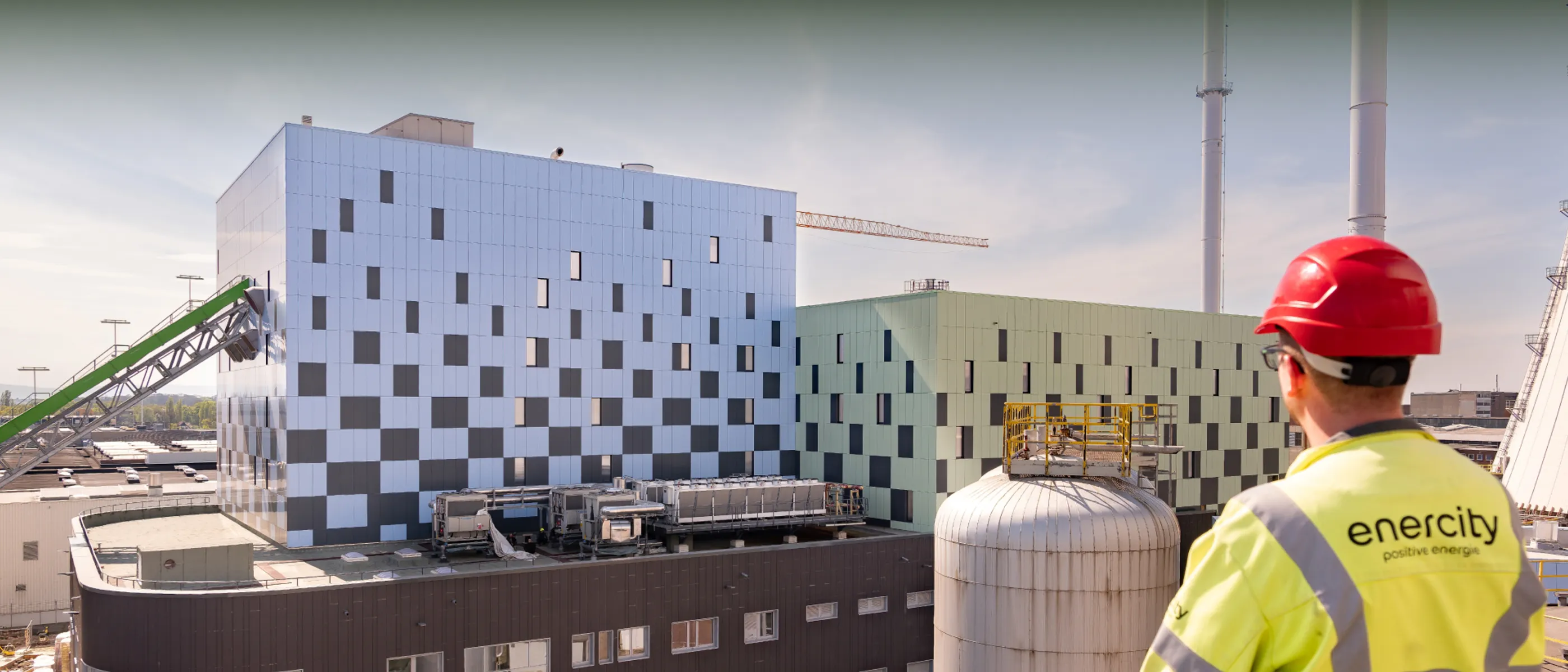 Ein Techniker in Schutzkleidung betrachtet eine große Industrieanlage mit Gebäuden und Schornsteinen.